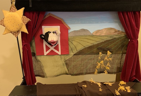 Puppet show stage showing a cow and a barn and a sun